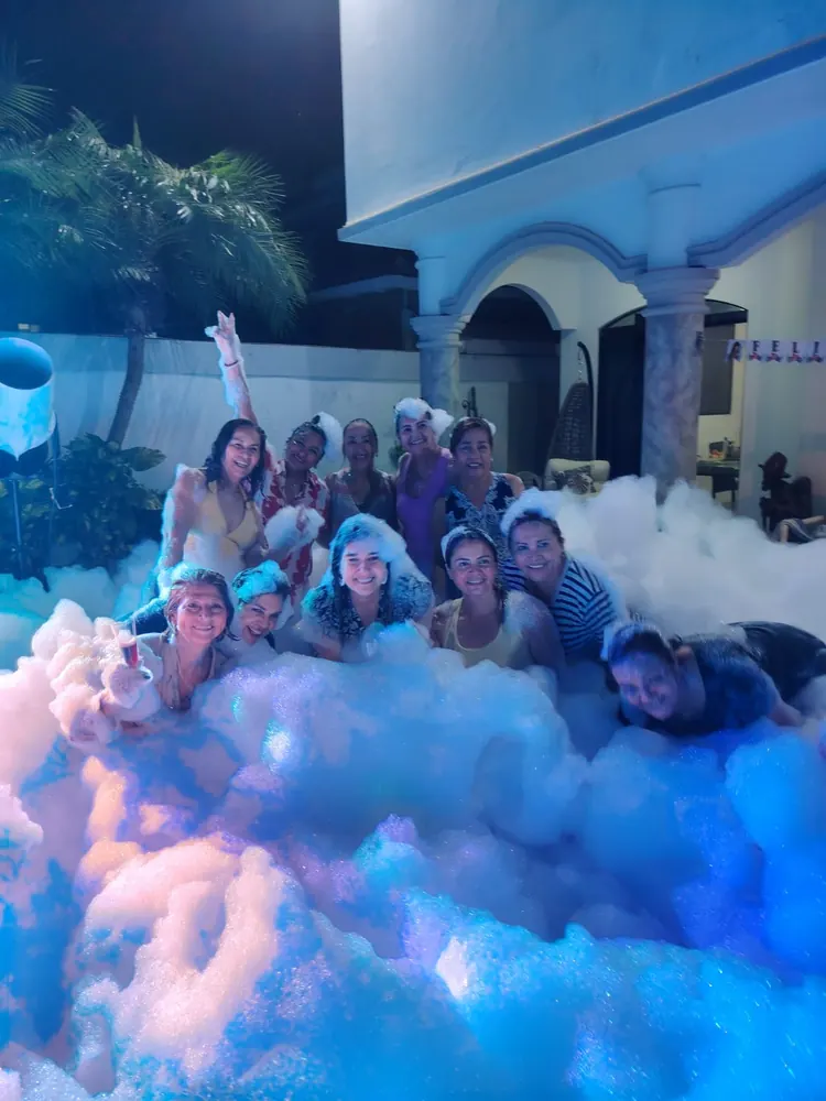 Grupo de amigas disfrutando una fiesta de espuma nocturna con luces en casa